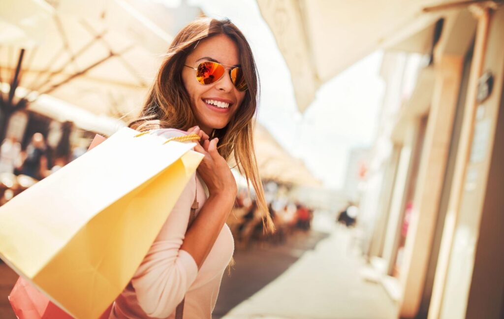 A person wearing mirrored sunglasses with outside, holding shopping bags over their shoulder.